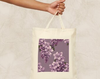 May include: A white canvas tote bag with a purple floral design. The flowers are a cluster of lilac blossoms with green leaves on a light purple background.