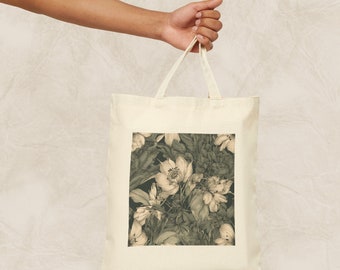 Op de afbeelding: Een beige canvas draagtas met een bloemenprint. Het ontwerp heeft een donkergroene achtergrond met witte bloemen en bladeren.