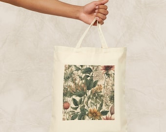Op de afbeelding: Een witte canvas tote bag met een bloemenprint met verschillende bloemen en bladeren in tinten groen, roze en geel.