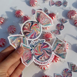 Może przedstawiać: Kolorowa naklejka z miętowym cukierkiem w kształcie spirali z brokatem. Naklejka ma kształt cukierka i zawiera tekst "Holiday Peppermint Candy" oraz adres strony internetowej.