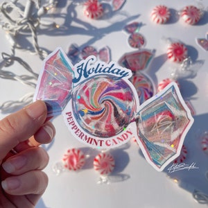 Może przedstawiać: Biała naklejka z kolorowym wzorem miętowego cukierka. Naklejka zawiera napis "Holiday Peppermint Candy" w czerwonych i niebieskich literach.