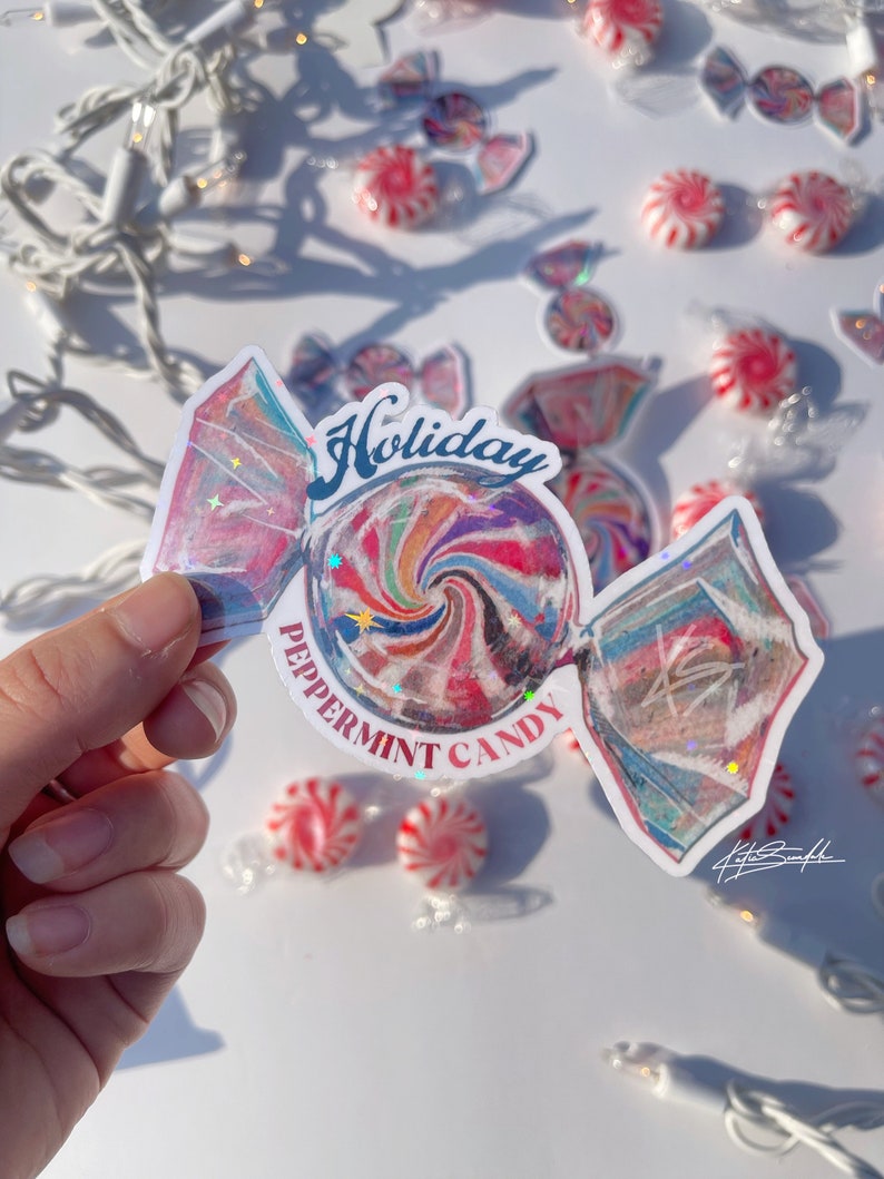 Może przedstawiać: Biała naklejka z kolorowym wzorem miętowego cukierka. Naklejka zawiera napis "Holiday Peppermint Candy" w czerwonych i niebieskich literach.