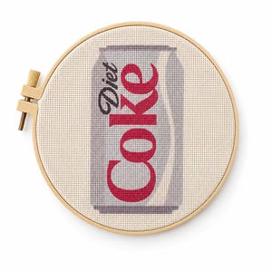 May include: A cross-stitch embroidery piece mounted in a circular wooden hoop, featuring a gray and white soda can design with the red text Diet Coke stitched onto a cream-colored fabric background, showcasing detailed needlework and texture.