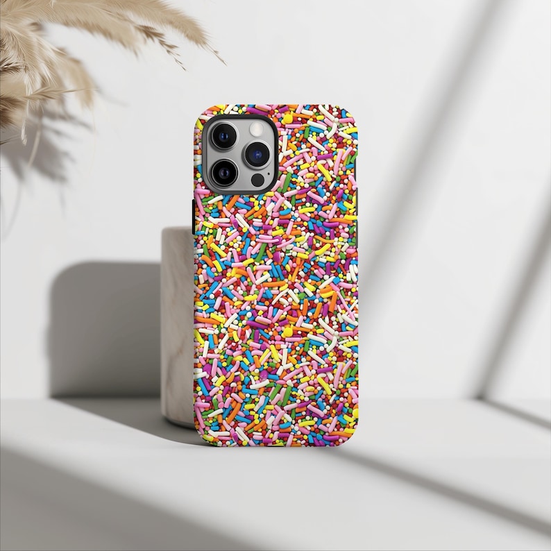 May include: A colourful phone case with a pattern of sprinkles. The case is designed for an iPhone with a camera bump.