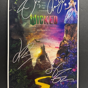 Puede incluir: Un cartel promocional del musical "Wicked" con el texto "You Will Be Changed" y "Wicked For Good". La imagen incluye ilustraciones de personajes y un camino de baldosas amarillas, con múltiples firmas.