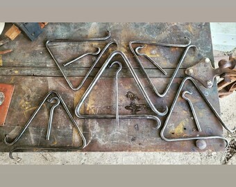 Puede incluir: Un conjunto de seis ganchos triangulares de metal con un gancho curvo en la parte superior. Los ganchos están dispuestos sobre una superficie de madera.