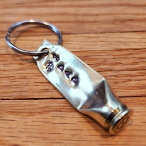 May include: A brass keychain shaped like a bullet casing with the word "#1 DAD" engraved on it. The keychain has a silver metal ring.