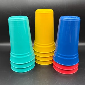 May include: A stack of colorful plastic cups in teal, yellow, blue, and red. The cups are stacked in a way that they can be nested together. The cups are made of a durable plastic material.