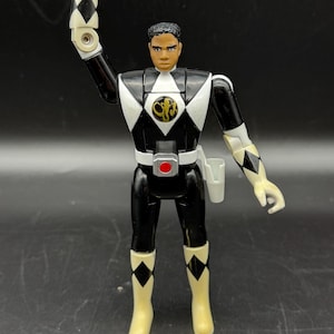 May include: A white ceramic mug with a black handle and the text "But First, Coffee" in a bold, black font. The mug is set against a blurred background, suggesting a cozy setting. The mug appears to be approximately 4 inches tall.