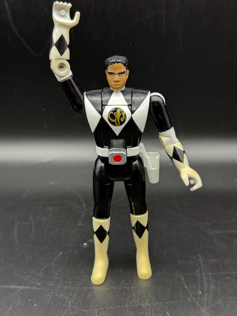 May include: A white ceramic mug with a black handle and the text "But First, Coffee" in a bold, black font. The mug is set against a blurred background, suggesting a cozy setting. The mug appears to be approximately 4 inches tall.