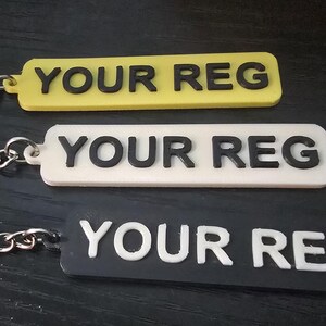 May include: Keychains in yellow, white, and black, each with the text "YOUR REG" in contrasting colors. The keychains have a rectangular shape and are attached to silver key rings with a chain.
