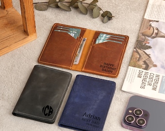 May include: An assortment of leather wallets in various colors. One brown wallet is open, displaying cards and cash, with "HAPPY BIRTHDAY DADDY" engraved. Other wallets are gray and blue, with personalized text and initials.