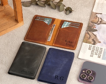 May include: Three leather wallets with different colors and personalized engravings. The top wallet is brown with the names "Kelvin Emma" engraved on it. The middle wallet is dark gray with the words "Love You" engraved on it. The bottom wallet is blue with the initials "R G" engraved on it.