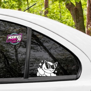 May include: A white vinyl decal applied to a car window featuring a stylised turtle character wearing sunglasses with small star accents. A second decal on the window displays the text MODIFIED CARS 74 in a pink and blue neon-style circular frame.