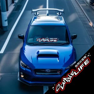 May include: A blue sports car with a rear spoiler, viewed from above, parked on a road. The car features the text "Subie Life" in a stylized font across the windshield, along with Japanese text.