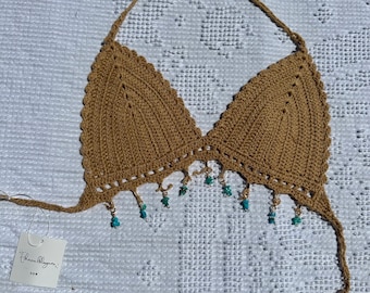 May include: A brown crocheted halter top with turquoise beads hanging from the bottom. The top has a tie closure at the back of the neck.