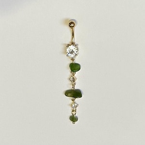 May include: Gold body jewelry with a clear crystal and three green stone accents.