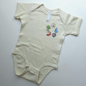 May include: A cream-colored short-sleeve baby bodysuit featuring a small graphic print on the chest. The design includes five distinct icons: a green tree, a white sun, a blue water droplet, a red flame, and a grey skull. A white tag is attached.