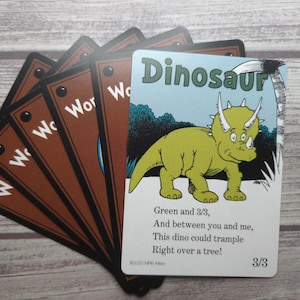 May include: A set of children's flashcards featuring a green triceratops dinosaur illustration. The card reads "Dinosaur" at the top, with a short poem and the number "3/3" at the bottom. The other cards are brown with the word "Wor" on them.