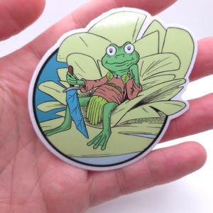 May include: A sticker featuring a cartoon frog with a sword, dressed in a brown shirt and green skirt, sitting on a large green leaf. The frog has large eyes and is holding a blue sword.