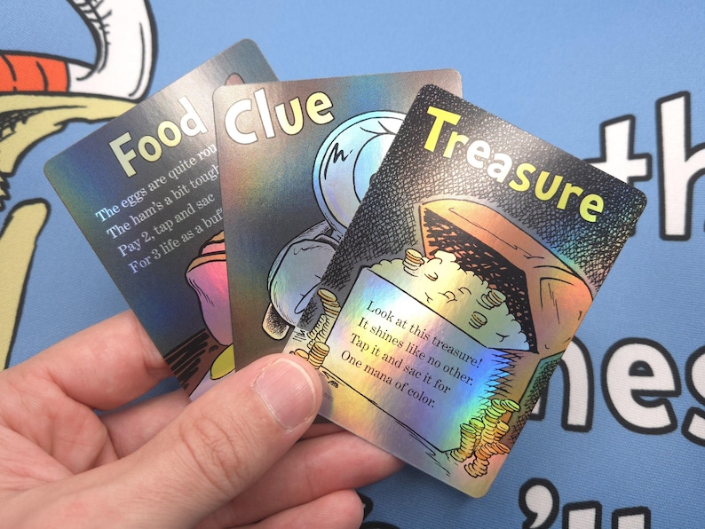 May include: Three holographic game cards with colorful illustrations and text. The cards are labeled "Food", "Clue", and "Treasure". The "Treasure" card shows a chest full of gold coins with the text "Look at this treasure! It shines like no other. Tap it and sac it for one mana of color."