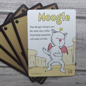 May include: A Moogle card with a white creature illustration, red wings, and the text "Moogle." The card has the text "This Moogle will give you life when they strike. Something opponents will really not like." The card is marked 1/2.