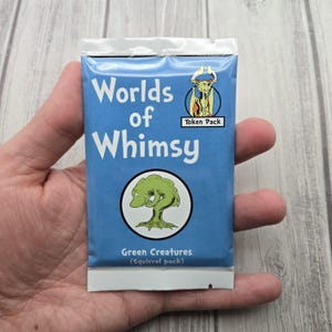 May include: A blue packet of "Worlds of Whimsy" token packs. The packet features white text and a circular graphic of a green creature. The text "Green Creatures (Squirrel pack)" is below the graphic. A small illustration of a horned creature is in the upper right corner.