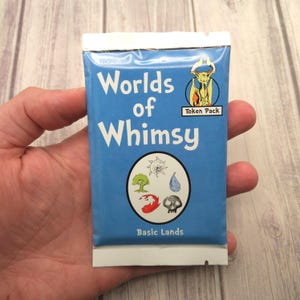 Könnte beinhalten: Ein blaues Päckchen mit der Aufschrift "Worlds of Whimsy" und "Token Pack". Es zeigt Illustrationen eines Baumes, eines Wassertropfens, eines Schädels und anderer Fantasy-Elemente. Das Päckchen wird in einer Hand gehalten.