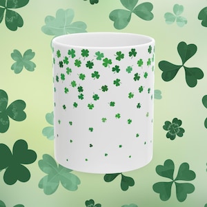 May include: White ceramic mug with a green shamrock pattern. The shamrocks are scattered randomly on the mug, with a higher concentration at the top and a lower concentration at the bottom.