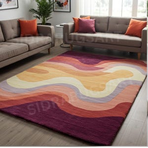 Puede incluir: Una alfombra rectangular grande con un diseño ondulado y abstracto. La alfombra presenta bandas de color en tonos de morado, rojo, naranja y crema. La alfombra está colocada sobre un suelo de madera en un salón.
