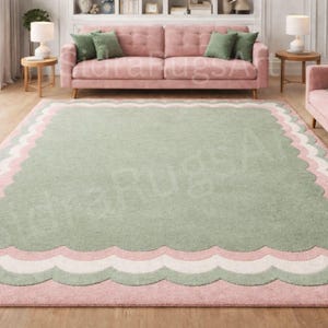 Puede incluir: Una alfombra rectangular grande con un borde festoneado. La alfombra presenta un centro verde claro, bordeado por capas de blanco, rosa y un borde festoneado rosa. La alfombra está en una sala de estar con sofás rosas y cojines verdes.
