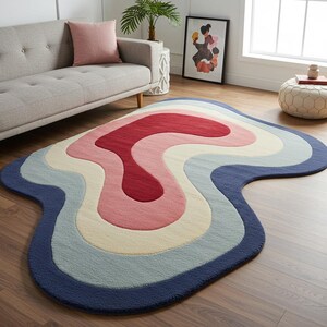 May include: A colorful, abstract area rug with a wavy, layered design. The rug features a palette of red, pink, cream, light blue, and navy blue. The rug is placed on a hardwood floor, adding a vibrant accent to the room.