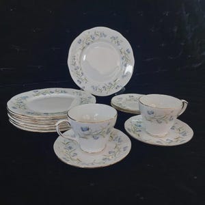 May include: A white porcelain tea set with a delicate blue floral pattern. The set includes teacups, saucers, and plates with gold trim. The plates are stacked, and the cups and saucers are arranged for display.