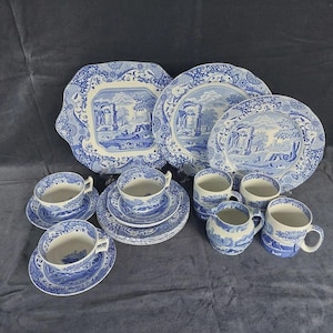 May include: A white ceramic mug with a black handle and the text "But First, Coffee" in a handwritten style. The mug is on a white surface. The mug is approximately 10 cm tall.