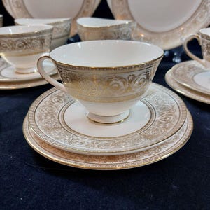 Pode incluir: Conjunto de chá branco elegante com detalhes em filigrana dourada. A chávena tem uma forma arredondada com uma pega delicada, e o pires apresenta um design ornamental a condizer. Parte de uma coleção maior de porcelana fina.