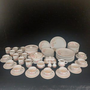 May include: A complete vintage floral dinner service in cream and pink. The set includes plates, bowls, cups, saucers, serving dishes, and a butter dish. The floral pattern is a delicate pink, with gold trim.