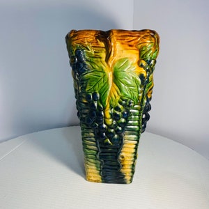 Puede incluir: Un jarrón de cerámica con forma rectangular y un diseño de uvas y hojas en tonos verdes, amarillos y azules.