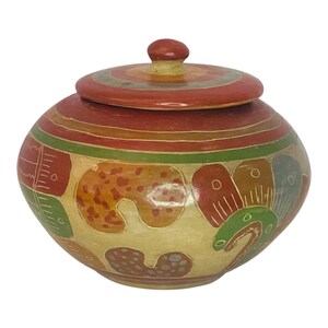 Puede incluir: Un tarro de cerámica pintado a mano con tapa. El tarro está decorado con coloridos patrones geométricos en tonos rojos, naranjas, verdes y azules. El tarro es una pieza tradicional de arte popular mexicano.