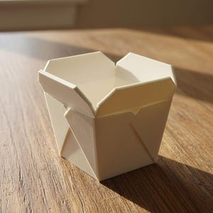 May include: A small, off-white, square-shaped container with four folding top flaps, mimicking the design of a traditional takeout box. The object features a smooth, matte surface with visible 3D printed layer lines throughout its structure.
