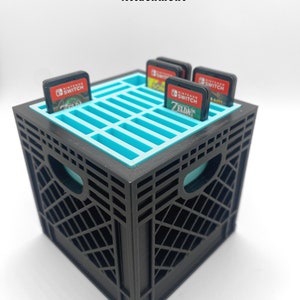 May include: Black plastic crate with a blue interior, designed to hold 24 Nintendo Switch game cartridges. The crate measures 3 inches by 3 inches by 3 inches.  The text "NINTENDO SWITCH" and "ZELDA" are visible on the game cartridges.