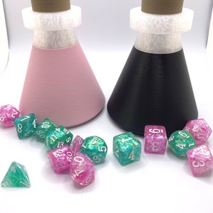 May include: Two conical glass bottles with cork stoppers and white lids, one pink and one black, with a scattering of green and pink dice with white numbers.