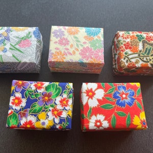 May include: Five small, square boxes with floral patterns. The boxes are made of paper and have a variety of colors and designs. The boxes are all closed and are arranged in a row.