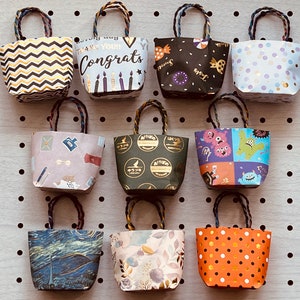 May include: Ten small gift bags with various patterns and designs. The bags are made of paper and have handles. The patterns include zigzags, polka dots, monsters, candles, and flowers.