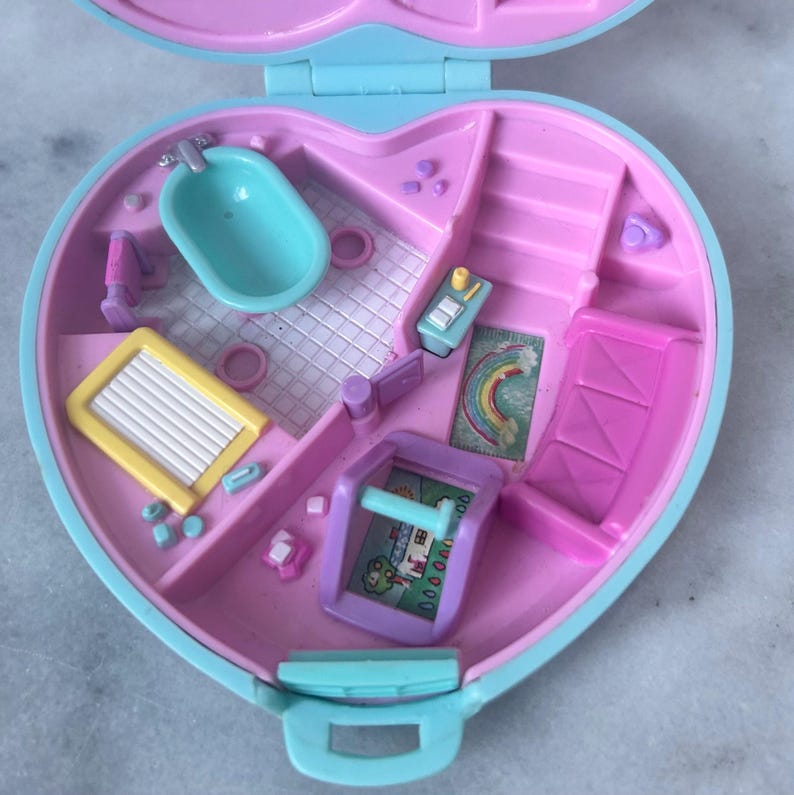 Pu&ograve; includere: Una casetta di giocattolo in plastica rosa e blu con una vasca da bagno, delle scale, un letto e un tappeto arcobaleno. La casa &egrave; aperta e l'interno &egrave; visibile.