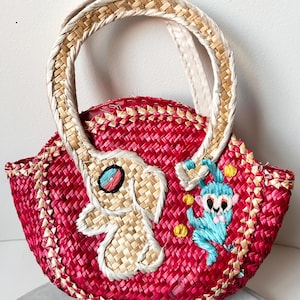 May include: A small, red woven straw bag with a white handle. The bag features embroidered details of an elephant and a monkey.