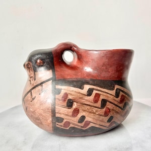 Puede incluir: Una olla de cerámica pintada a mano con un diseño geométrico marrón, rojo y negro. La olla tiene un asa única con un agujero.