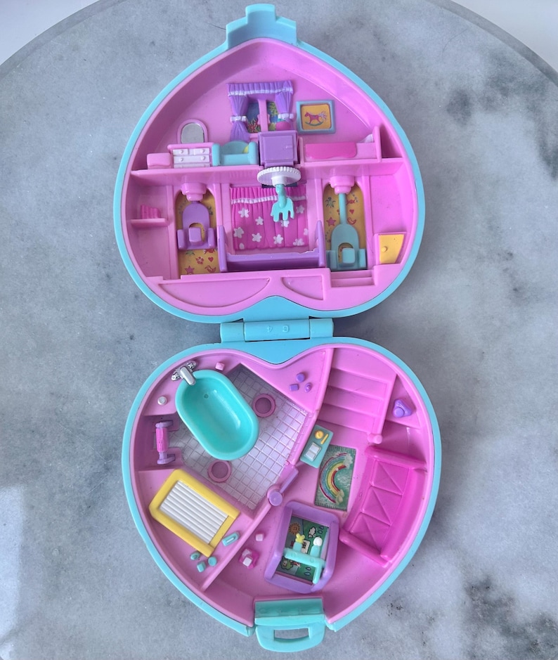 Pu&ograve; includere: Una casetta di giocattolo in plastica rosa e blu a forma di cuore. La casa &egrave; aperta e mostra l'interno, che &egrave; decorato con mobili e accessori. La casa &egrave; un set di gioco per piccole bambole o figurine.