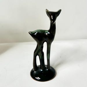 以下が含まれることがあります： 光沢のある濃い緑と黒の仕上げが施されたセラミック製の鹿の置物。鹿は細い体、長い脚、小さく丸みを帯びた台座をしています。この置物は装飾品です。
