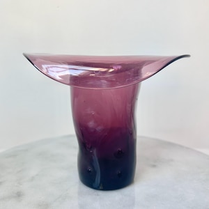 May include: A purple glass vase with a wide, flared opening and a twisted, textured body.