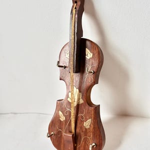 Könnte beinhalten: Ein hölzerner, geigenförmiger Schlüsselhalter mit goldenen floralen Einlagen und fünf Haken. Der Schlüsselhalter ist braun und hat eine Schnur, die in der Mitte verläuft.